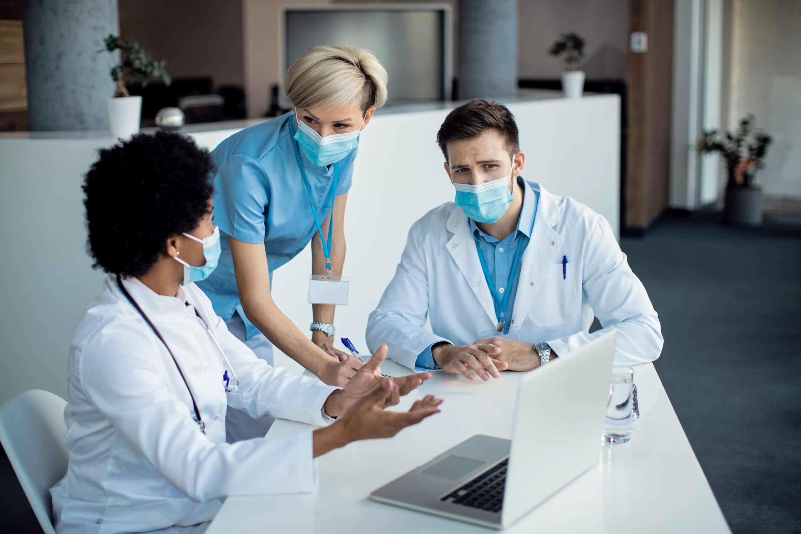 group-medical-experts-talking-while-using-laptop-during-meeting-hospital